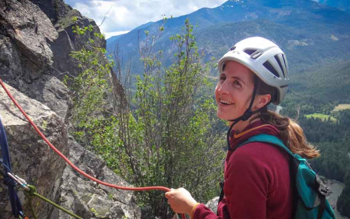 a rock climber smiles with mountains in the background